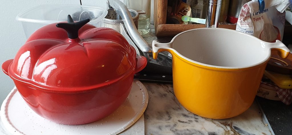 Le Creuset cooking ware with red tomato shaped casserole on left and orange open pot with no lid of right
