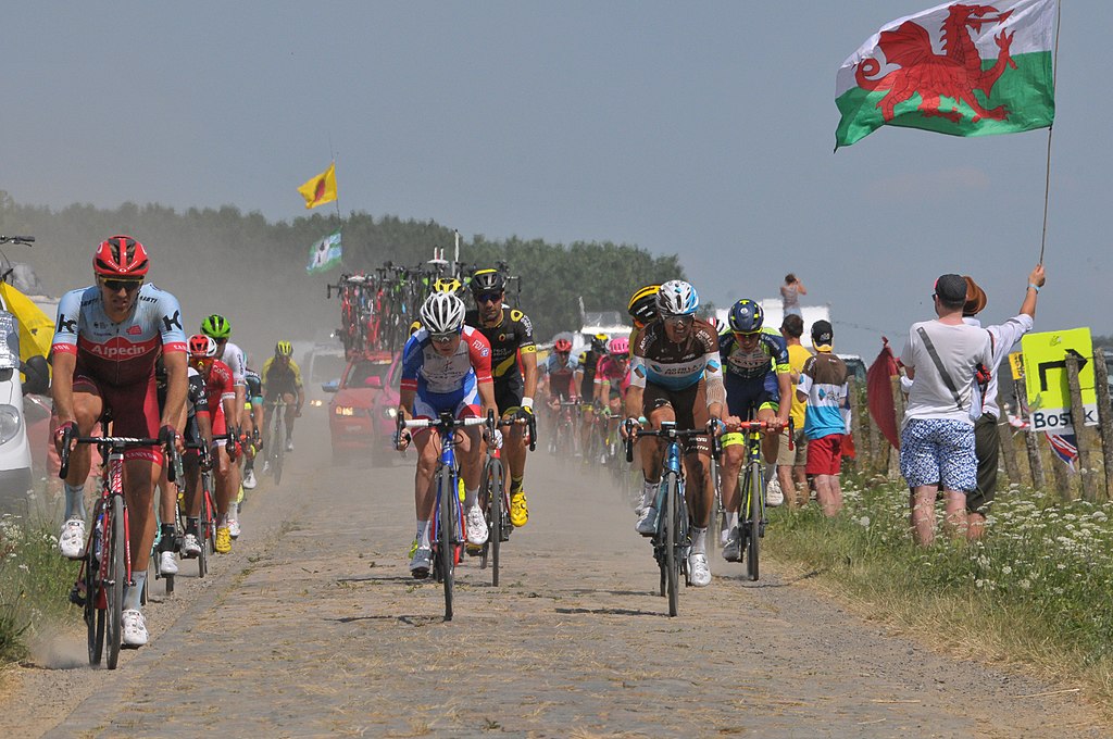 Tour de France 2018 with cyclist riding towards camera and man on right with Welsh flag