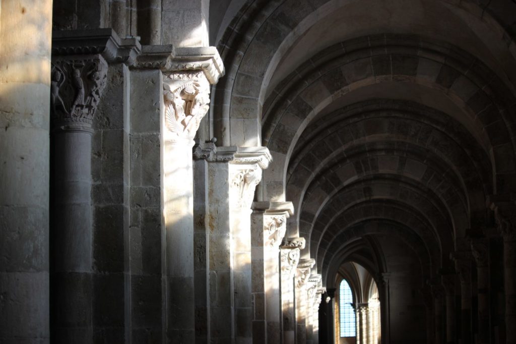 Interior of Vézelay basilica with light shining onto carved stone faces on the capitols