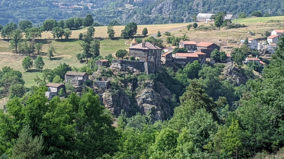 View from above down on an Auvergne village perched on a rocky hillside. Old chateau and stone houses with red tiled rooves