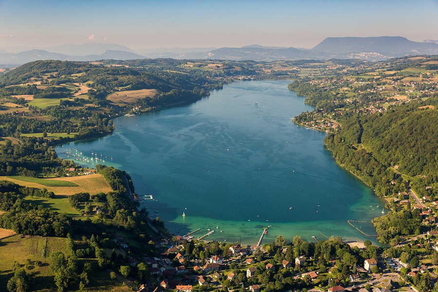 Aerial view of Lake Paladru. Huge lake stretching into distance with town in front and banks alon river with towns, roads, hills