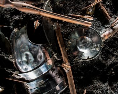 Battered Medieval weapons lying on earth: helmets and bits of wood