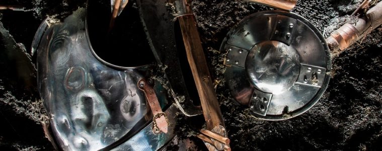 Battered Medieval weapons lying on earth: helmets and bits of wood