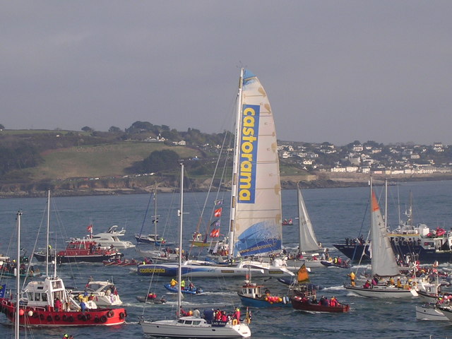 Ellen MacArthur arriving in Plymouth after her round the world singlehanded record with lots of small boats around her with her mast dwarfing them and headland with green grass in background