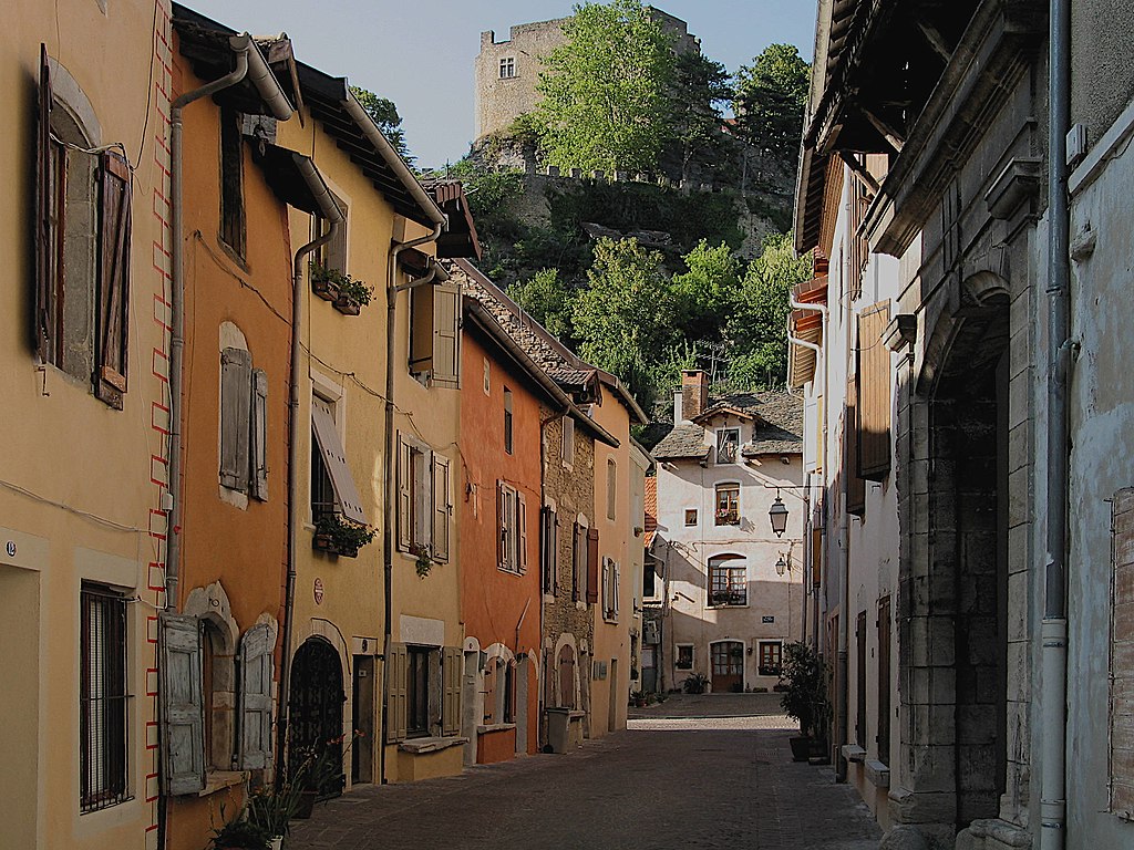 Crémieu medieval village with view down narrow streets with orange, red and ochre coloured houses on each side and mountain in background