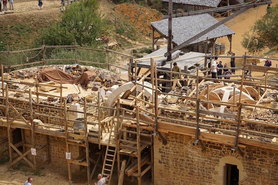 View from above of masons working on the walls at Guédelon medieval castle. Huge amount of large stones, men working with wooden machinery to raise top stone