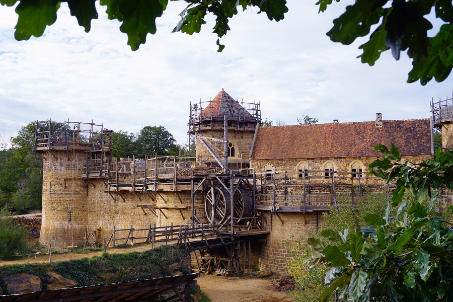View of front entrance of medieval castle at Guédelon showing wooden scaffolding on towers and walls, and tower behind with raised entrance over dry ditch