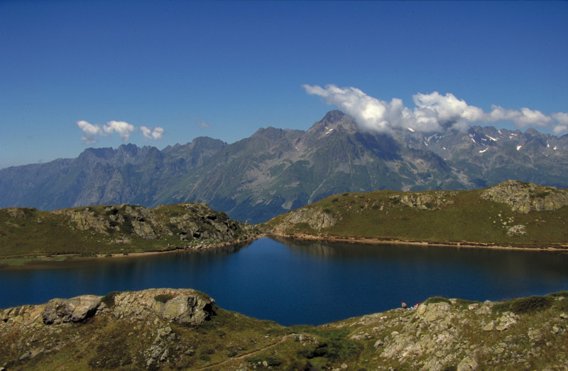 Dark blue mountain lake in Oisans with green shore in front and around lake and mountains in background