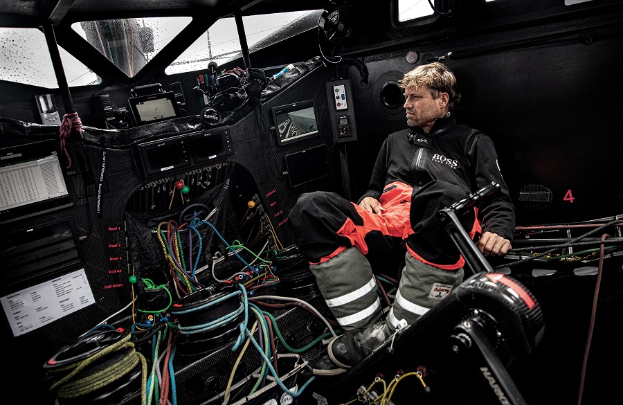Alex Thomson in the Vendee Globe 2020 race in his cockpit, which is covered operating what looks like a machine, with cables, and handles everywhere!