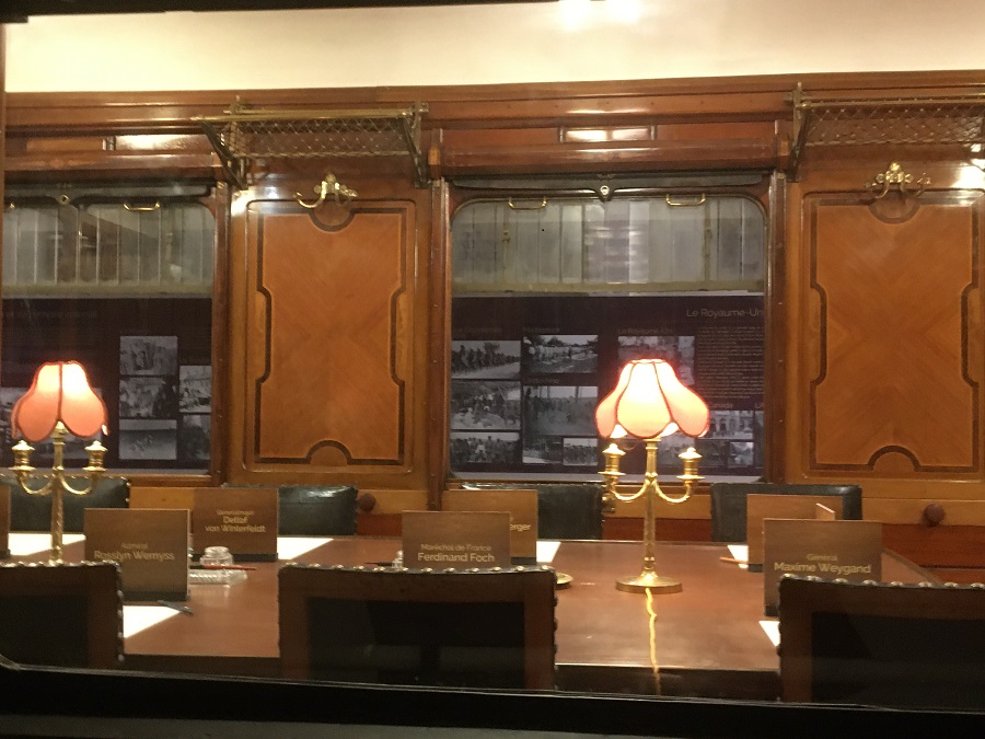 Looking into Armistice Museum railway carriage where the peace was signed in 1918 showing seats marked with names of those in the carriage, wooden walls and brass lamps