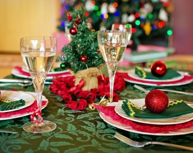 Tables laid for christmas with decorated tree in background, and table with green cloth, red baubles and ribbon and glasses of champagne