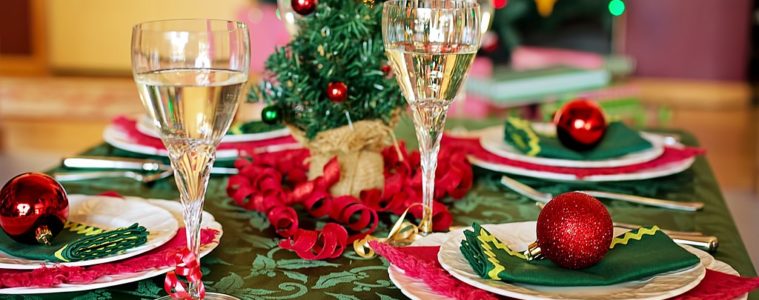 Tables laid for christmas with decorated tree in background, and table with green cloth, red baubles and ribbon and glasses of champagne
