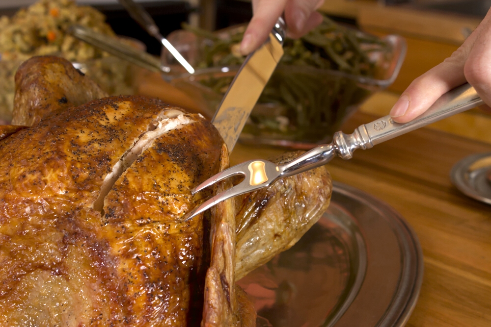 close up shot of whole turkey with person carving it showing hands holding knife and traditional carving fork