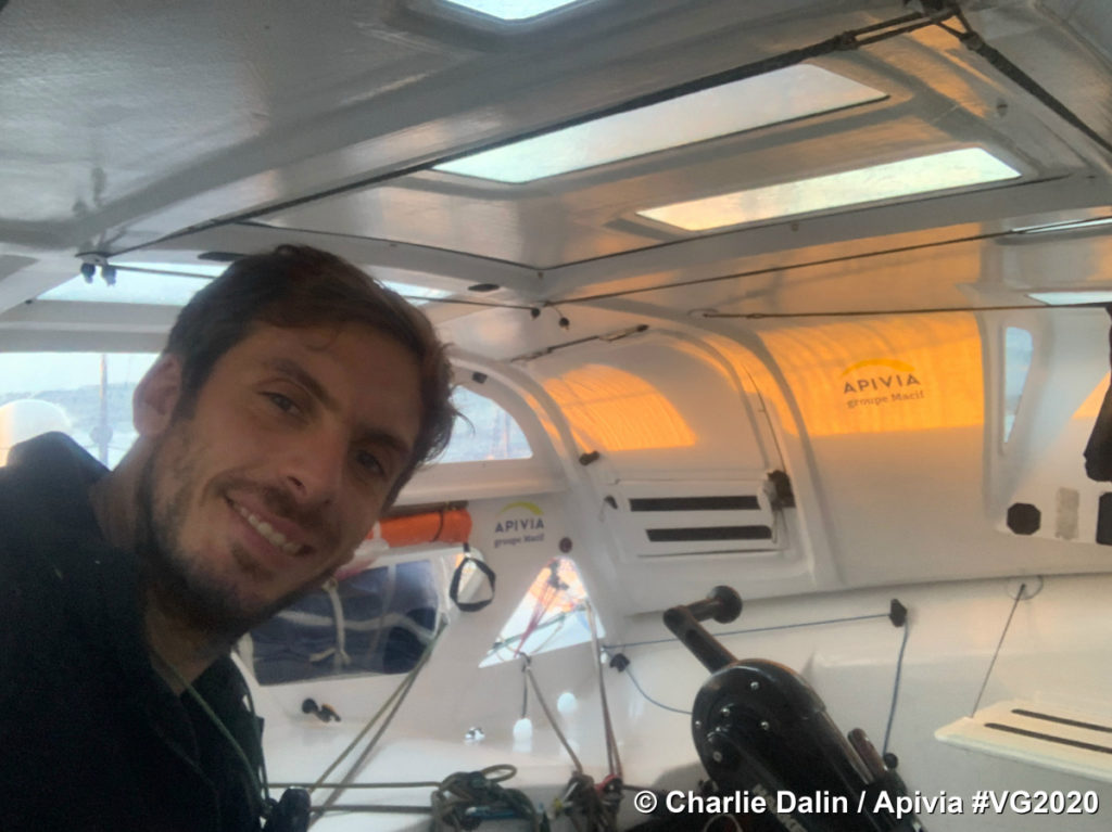 Chalie Dalin in Apivia with him looking at camera on left inside cosy looking boat with clear skies and yellow sunset behind