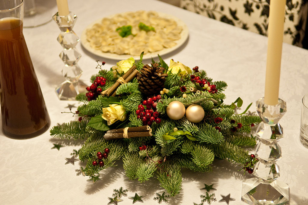 French christmas table decoration with wreath of pie and fir twigs with gold baubles on table with plate of food behind and crystal candlestick