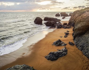 Veloroute beside the sea with shore on right with rocks on sand and rocky cliff face and rocks partly submerged inthe surf