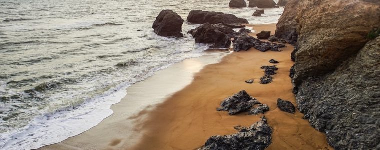 Veloroute beside the sea with shore on right with rocks on sand and rocky cliff face and rocks partly submerged inthe surf