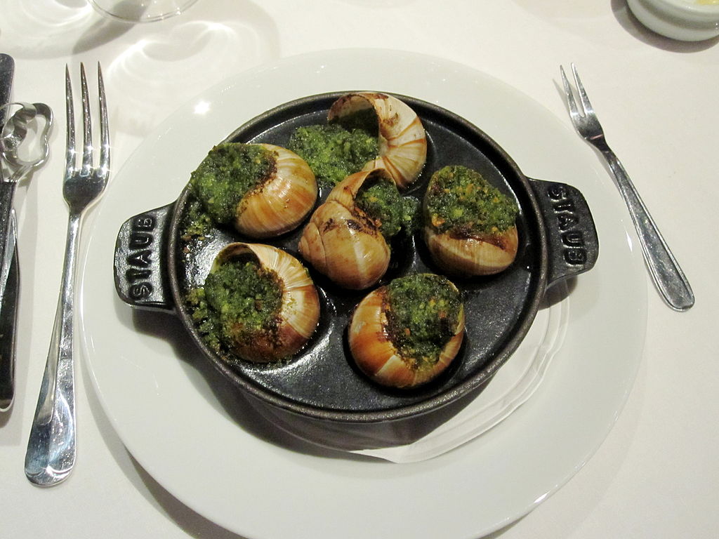 Special shaped iron dish of snails cooked with parsley and garlic on white background