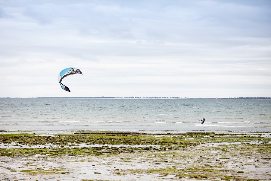 Kite surfing in Vendee with beach, with sand grass in front, sea behind and kite surfer in distance being pulled along by big kite