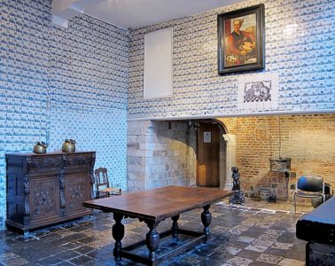Musee de l'Hospice museum in Lille. Kitchen with walls covered in blue tiles, bit fireplace, wooden furniture and wooden table in middle