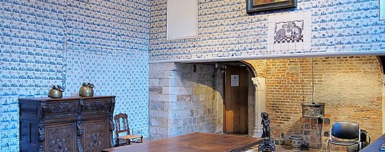 Musee de l'Hospice museum in Lille. Kitchen with walls covered in blue tiles, bit fireplace, wooden furniture and wooden table in middle