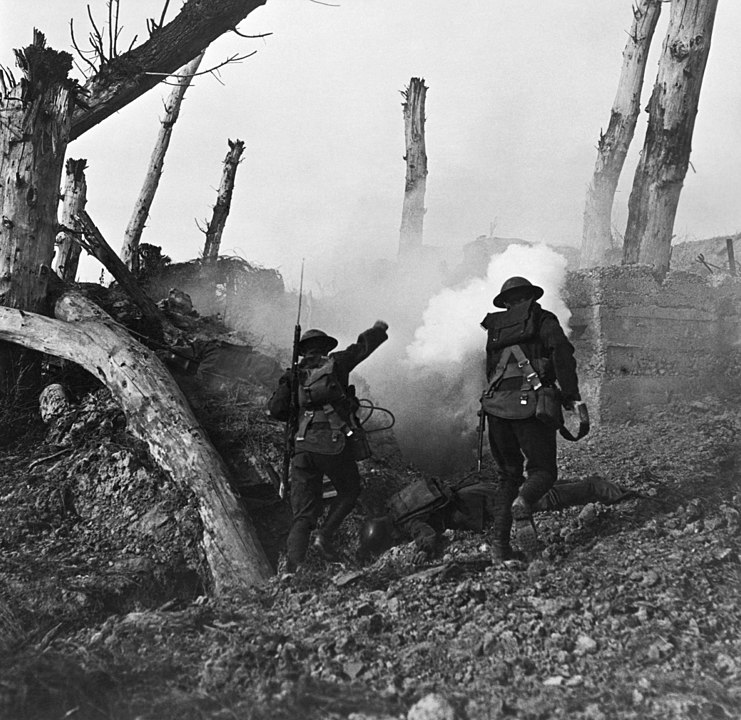 Black and white photo of 2 American soldiers running towards firing with backs to us, showing blasted trees aabove muddy tranch