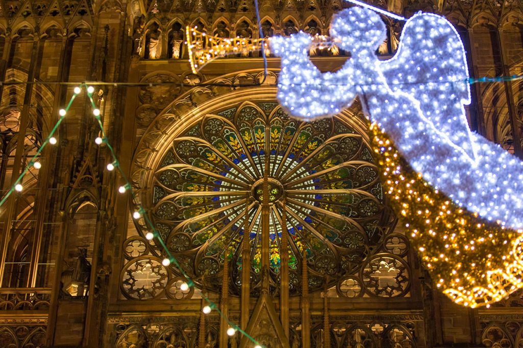 Illuminated flying angel playing trumpet lit up to right of Strasbourg Cathedral at Christmas with found window lit up behind