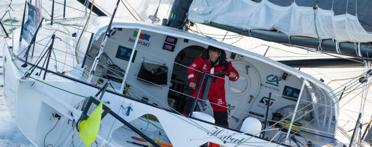 Jean Le Cam on his boat with pic from back showing him in main part of boat leaning sideways in sea spray