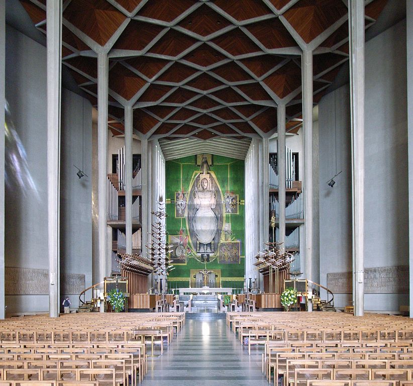 Graham Sutherland tapestry in coventry Cathedral looking down the nave from the back with tall concrete pillars oneither side and the huge tapestry of Christ above the altar at the end on green background