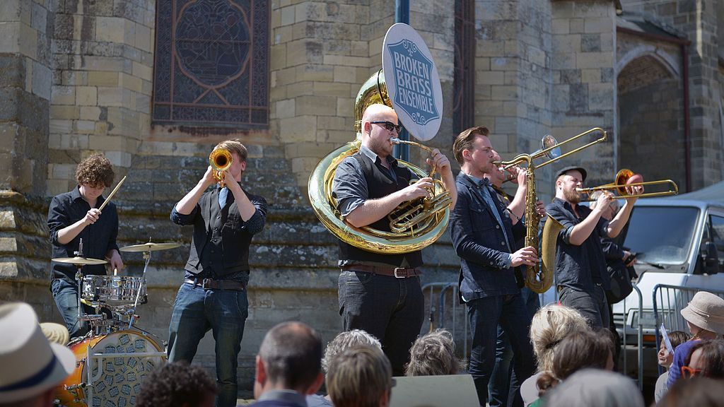 Jazz sous les Pommiers in Normandy festival with street band in front of crowd with church behind. One man with tuba wrapped around him, plus others playing brass instruments