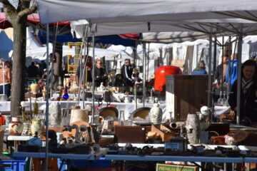 L'Isle-sur-la-Sorgue antiques fair showing very well stocked stand with candlesticks, pottery etc and people passing behind