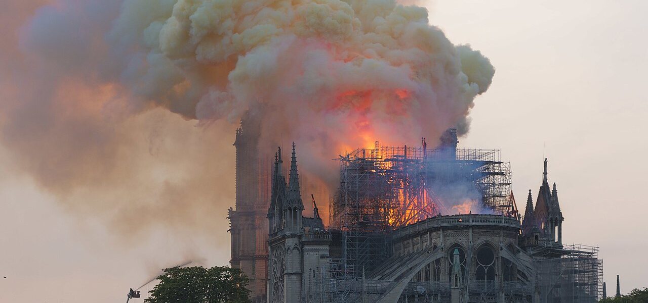 Notre-Dame de Paris on fire with smoke and flames from roof taken from behind some people watching the fire