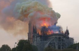 Notre-Dame de Paris on fire with smoke and flames from roof taken from behind some people watching the fire