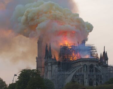 Notre-Dame de Paris on fire with smoke and flames from roof taken from behind some people watching the fire