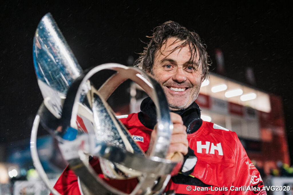 Yannick Bestaven with winner's trophy in sailing gear at night