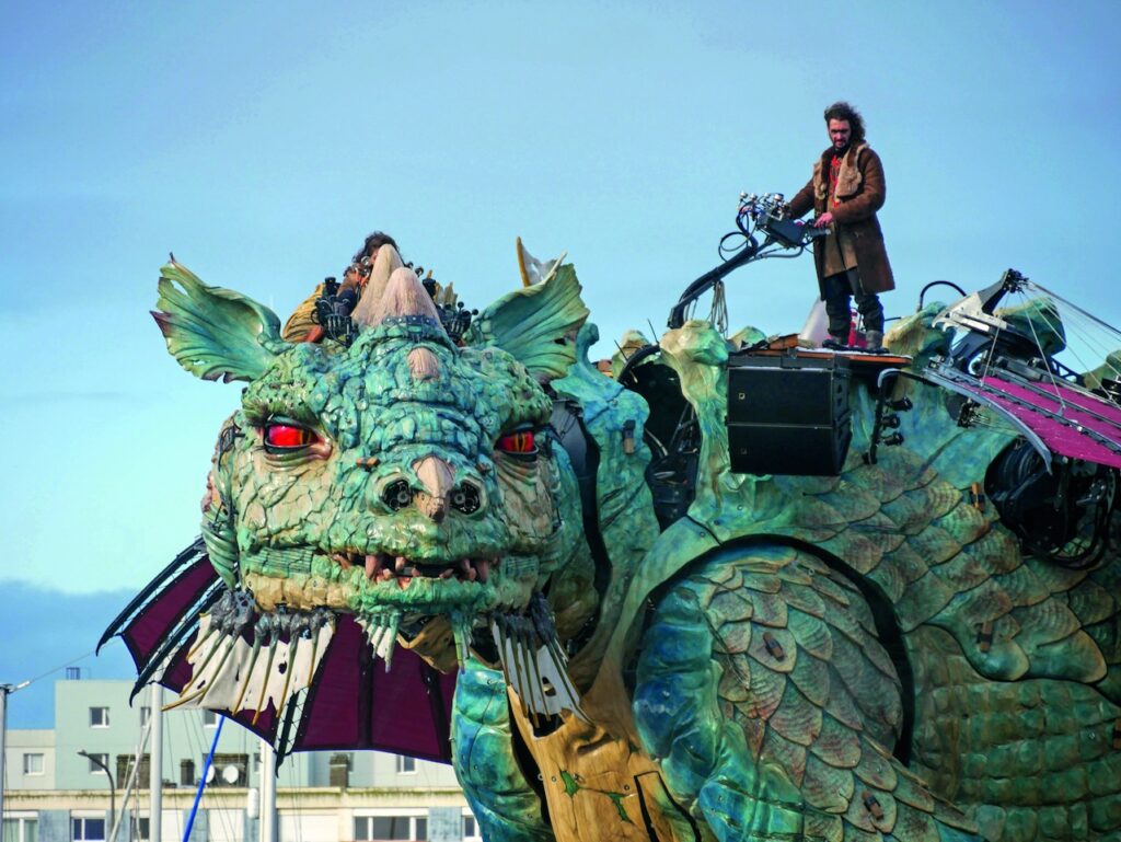 Calais Dragon vast mechanical beast looking to the camera with many on top who operates him via wheel that looks like out of Jules Verne