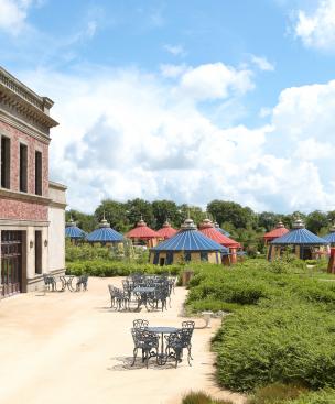 Shot of classical building to left, terrace with tables and in background round blue and gold tents at Puy du Fou theme hotel Field of the Cloth of Gold