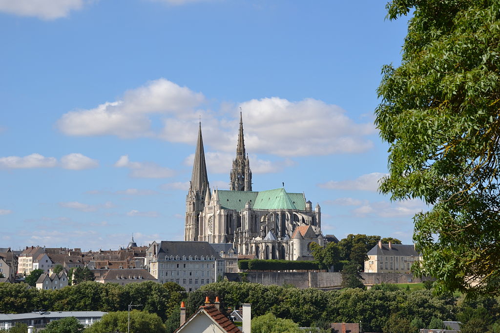 Chartres cathedral seen from afar in the town right on top of hill with trees to right and clouds behind the twin towers