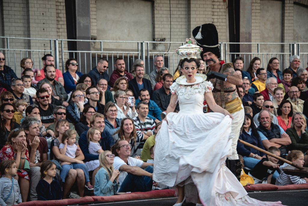 Comic lady in white dress performing in front of seated crowd at Le  Channel in Calais