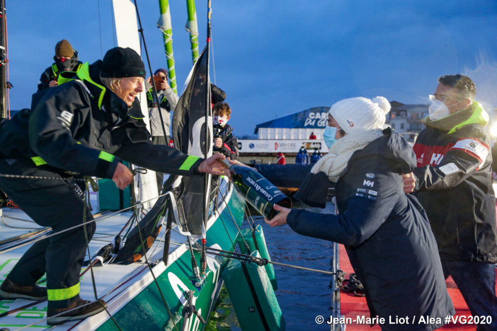 Miranda Merron finishes the Vendee Globe showing her on boat to left and people congratulating on right