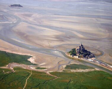 Aerial very long shot view of Mont St Michel in Nromandy showing sand banks and sea and green mainland and Mont St Michel island marooned
