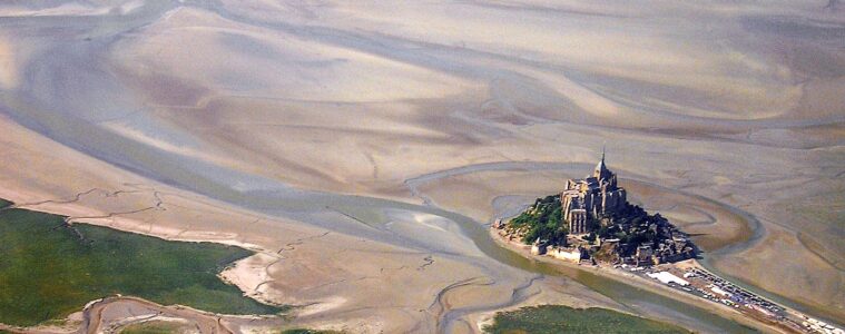Aerial very long shot view of Mont St Michel in Nromandy showing sand banks and sea and green mainland and Mont St Michel island marooned