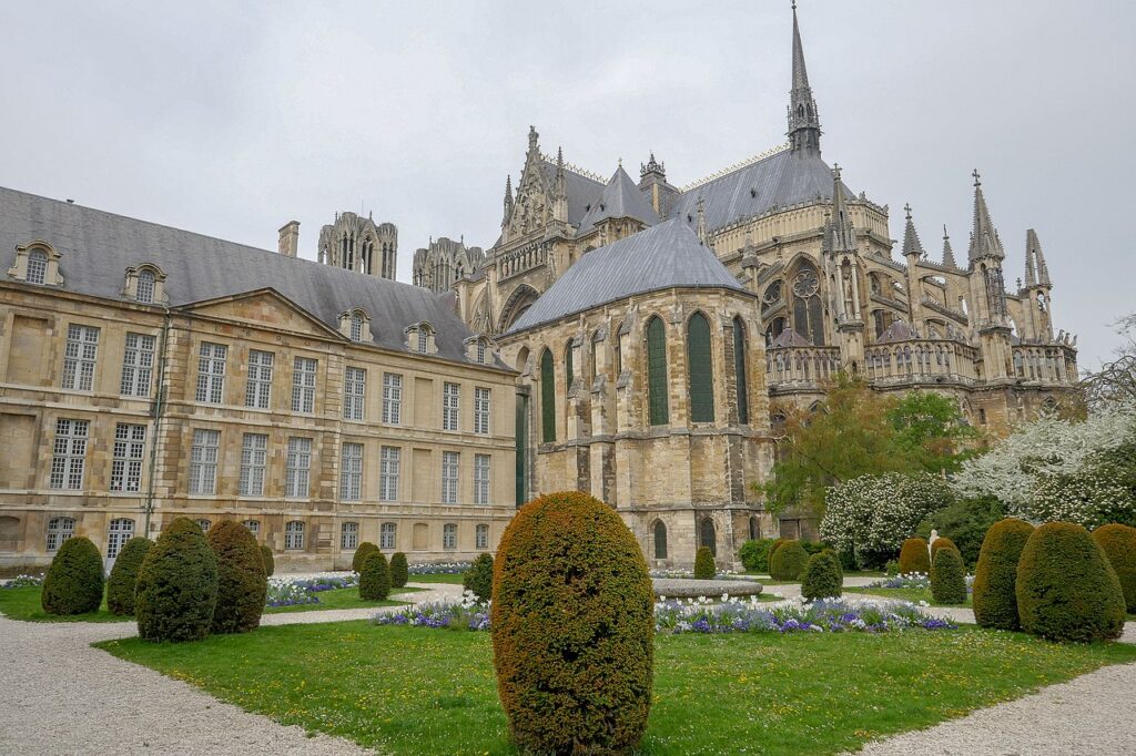 Reims Cathedral standing high in background behind ornate neo-classicalPalace de Tau and green garden in front