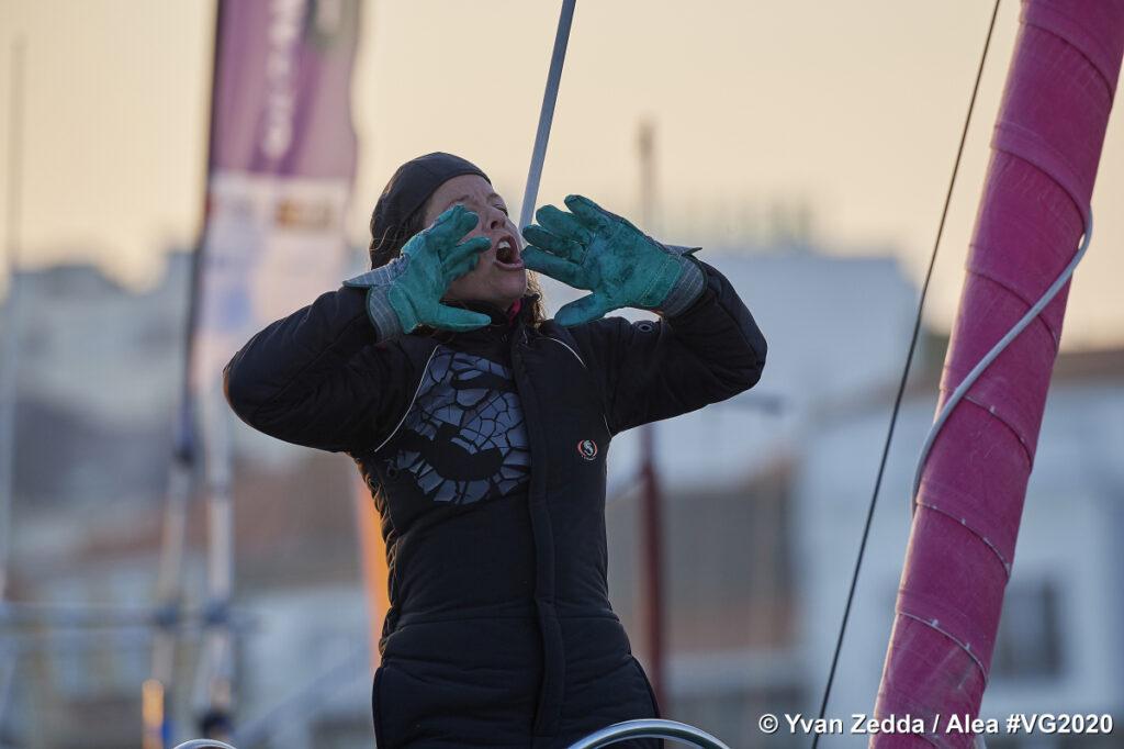 Alexia Barrier on board at the finish of the Vendee Globe race with hands up tomouth and shouting a message with blurred background of her boat