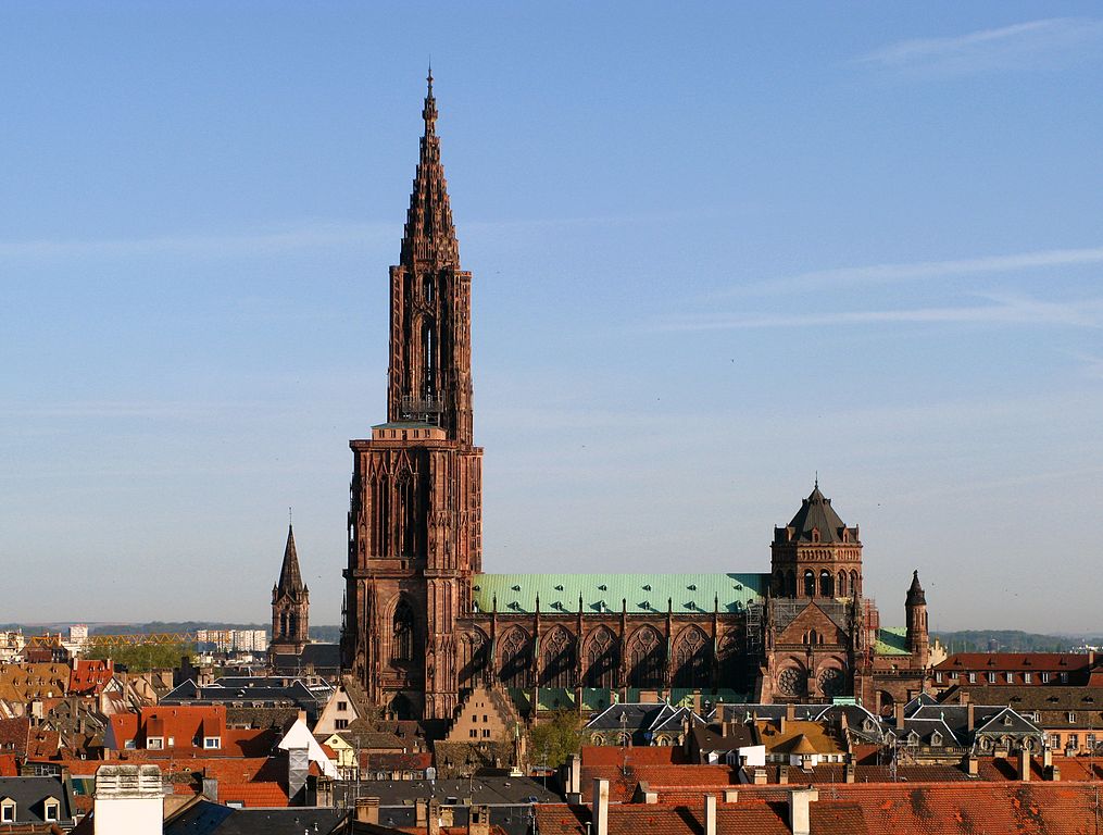 Strasbourg Cathedral from a little further away showing red rooves of the town and the very high spire and tower and nave with copper roof of the cathedral standing high above the city