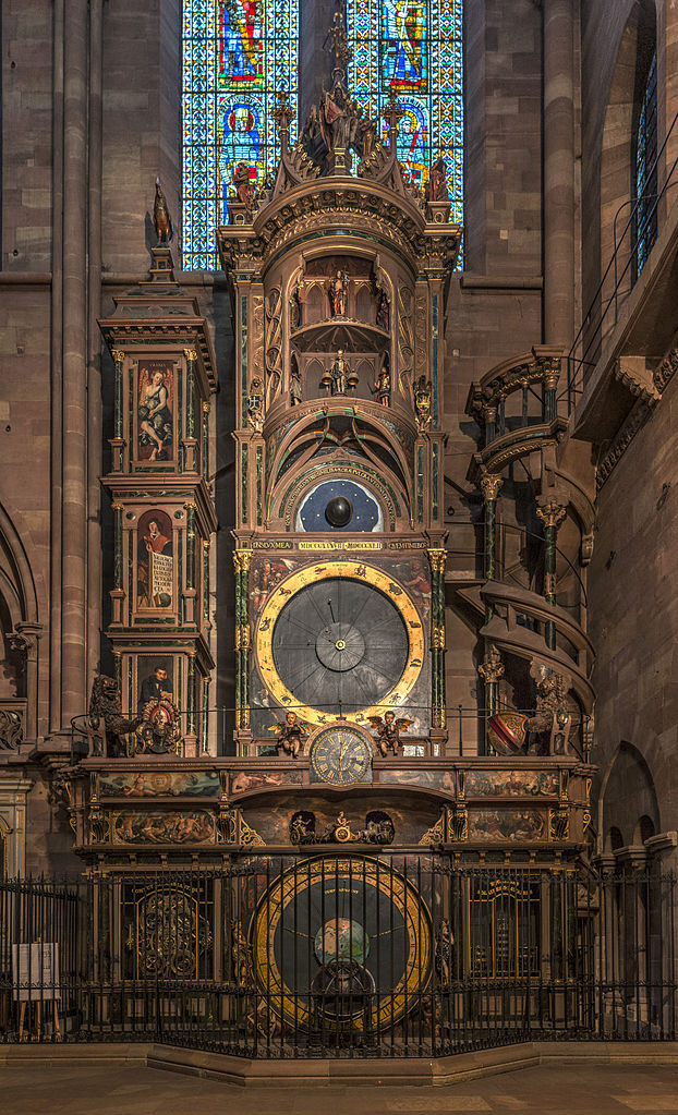 Astronomical clock in Strasbourg Cathedral. Multi tiered with elaborate clock face at bottom and three tiers above in red stone cathedral
