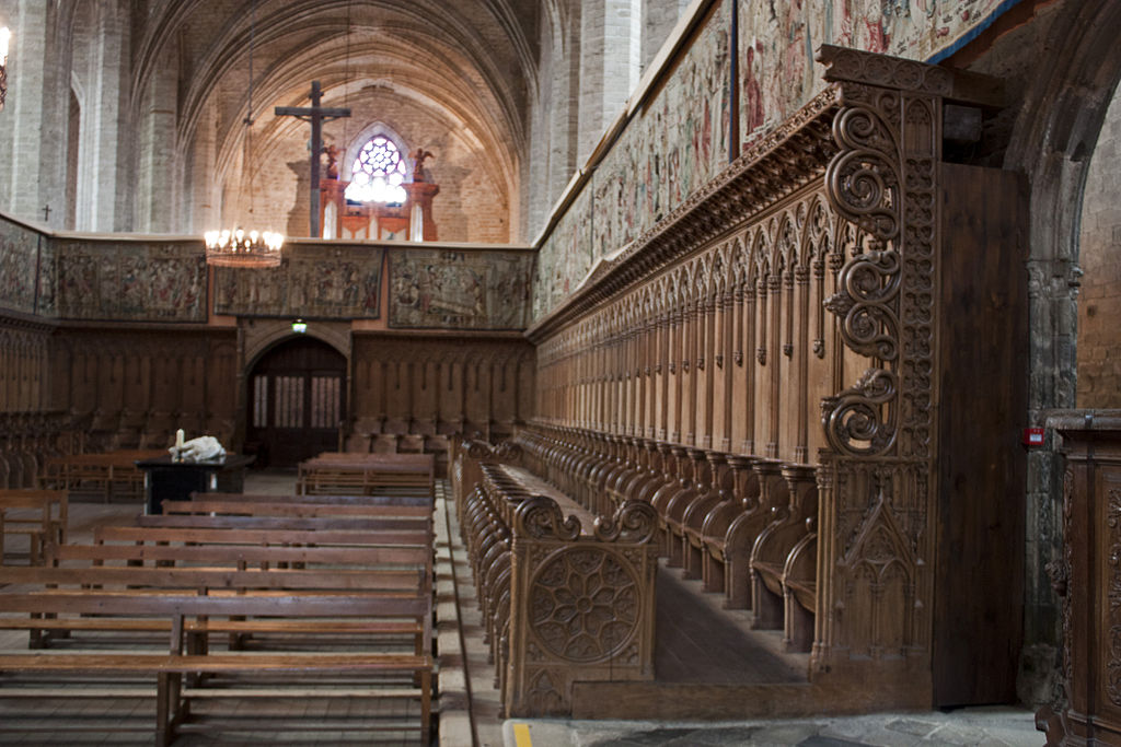 Abbey at La Chaise-Dieu withlong view down wooden choir stalls hightly decorated and cross above altar at end with arches and window lit behind