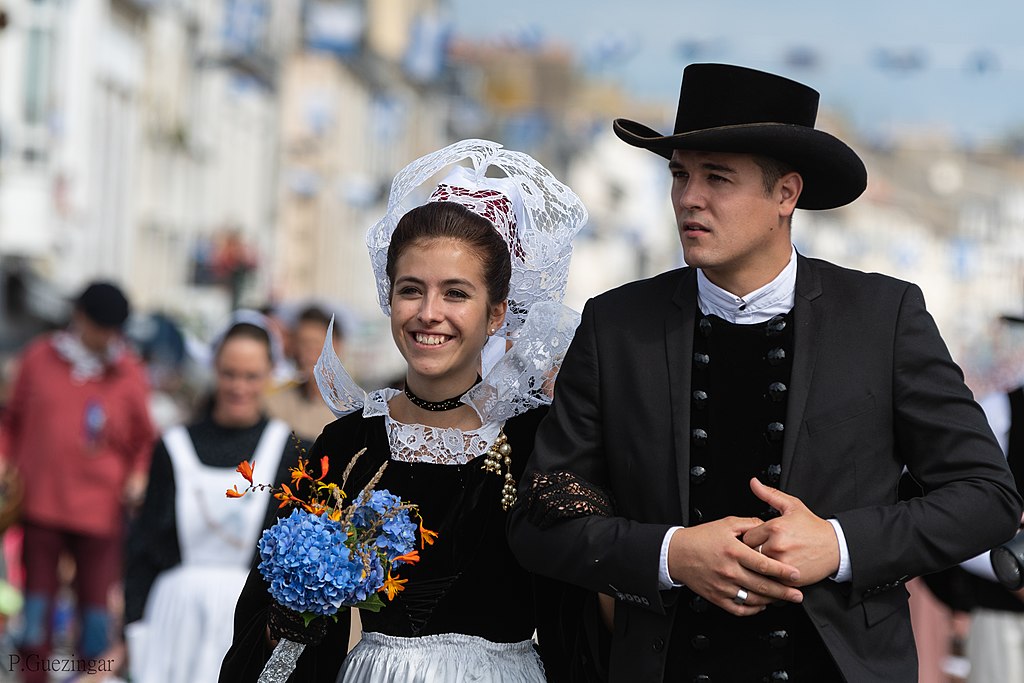 Filets Bleus Festival in Brittany with couple dressed in traditional Breton costume; she with black bodice and white apron with lwhite lace headdres; he with bit black hat, black clothes and white collar