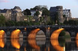 Angers bridge at sunset lit up under the arches reflected in the river with bridge and town beyond
