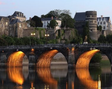 Angers bridge at sunset lit up under the arches reflected in the river with bridge and town beyond